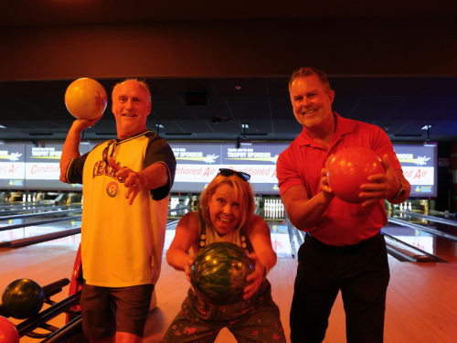 Three smiling attendees pose with colorful bowling balls at the 2025 Pins & Purpose event.
